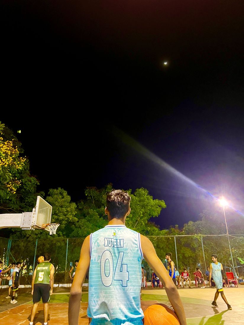Nuthan in his number 04 jersey holding a basketball on a floodlit court at night